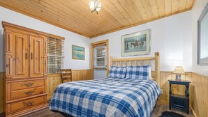 A bedroom with a wooden ceiling, a large bed with a blue and white checkered bedspread, a wooden wardrobe, a small table with a lamp, and a framed picture on the wall. - Cabin 3, Aspen Leaf Lodges, Near Grand Lake (Grand Lake)