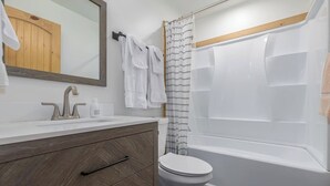 A modern bathroom with a wooden vanity, a white toilet, and a bathtub with a shower curtain. - Cabin 3, Aspen Leaf Lodges, Near Grand Lake (Grand Lake)
