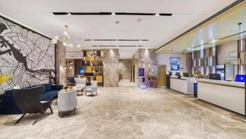 A hotel lobby with a reception desk, seating area, and a large wall mural.