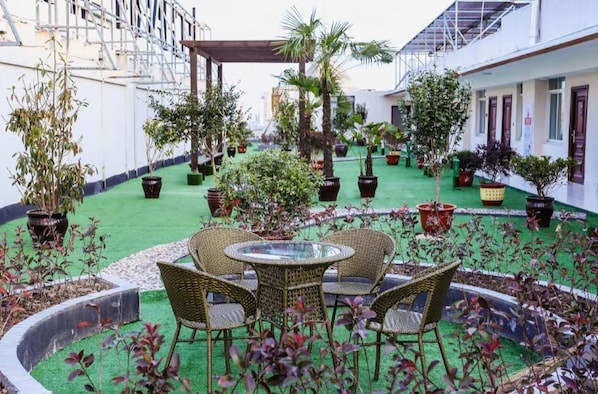 A courtyard with a round table and chairs, surrounded by potted plants and a green artificial turf area.