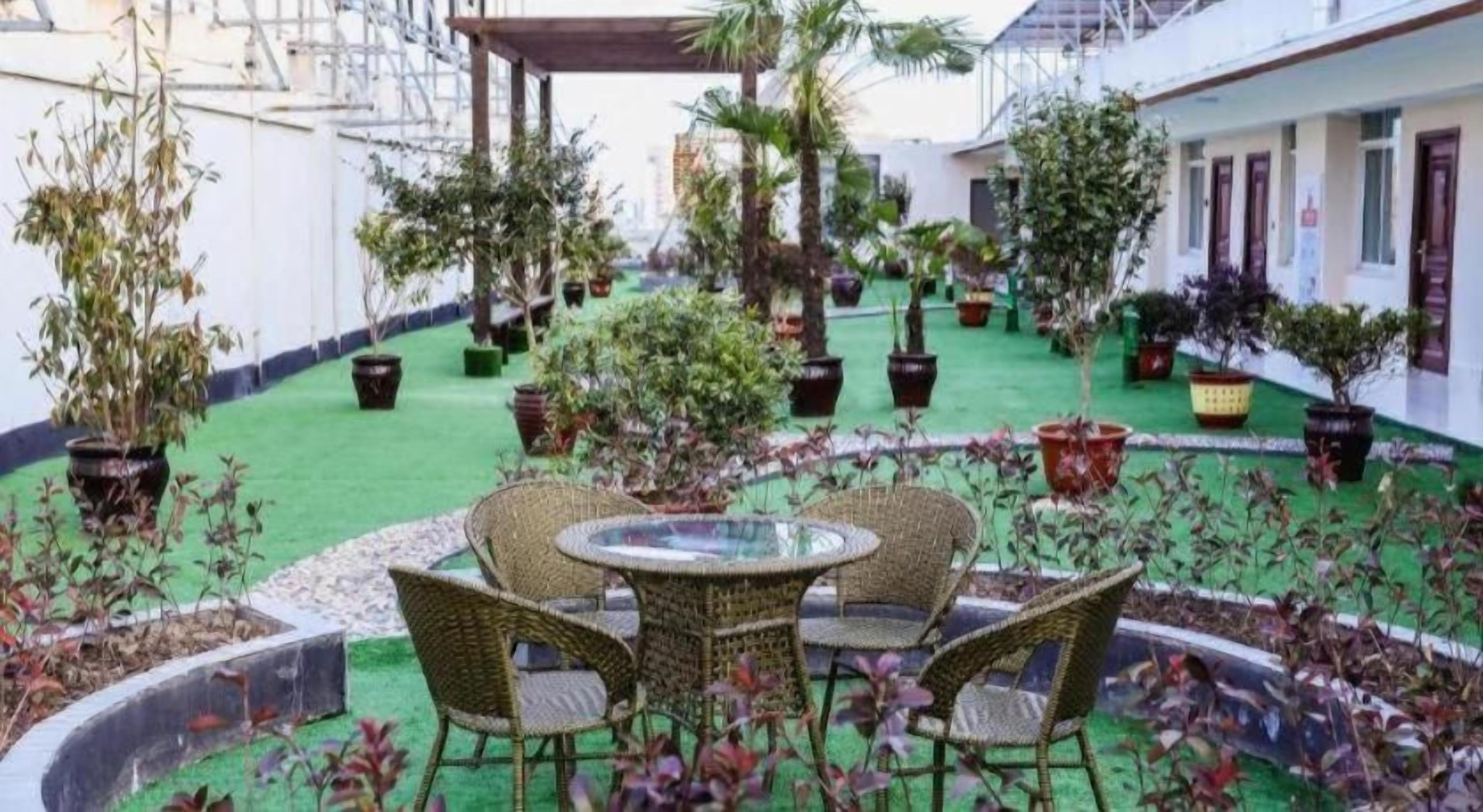 A courtyard with a round table and chairs, surrounded by potted plants and a green artificial turf.