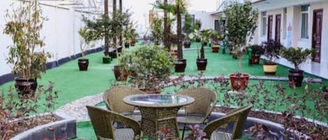 A courtyard with a round table and chairs, surrounded by potted plants and a green artificial turf.