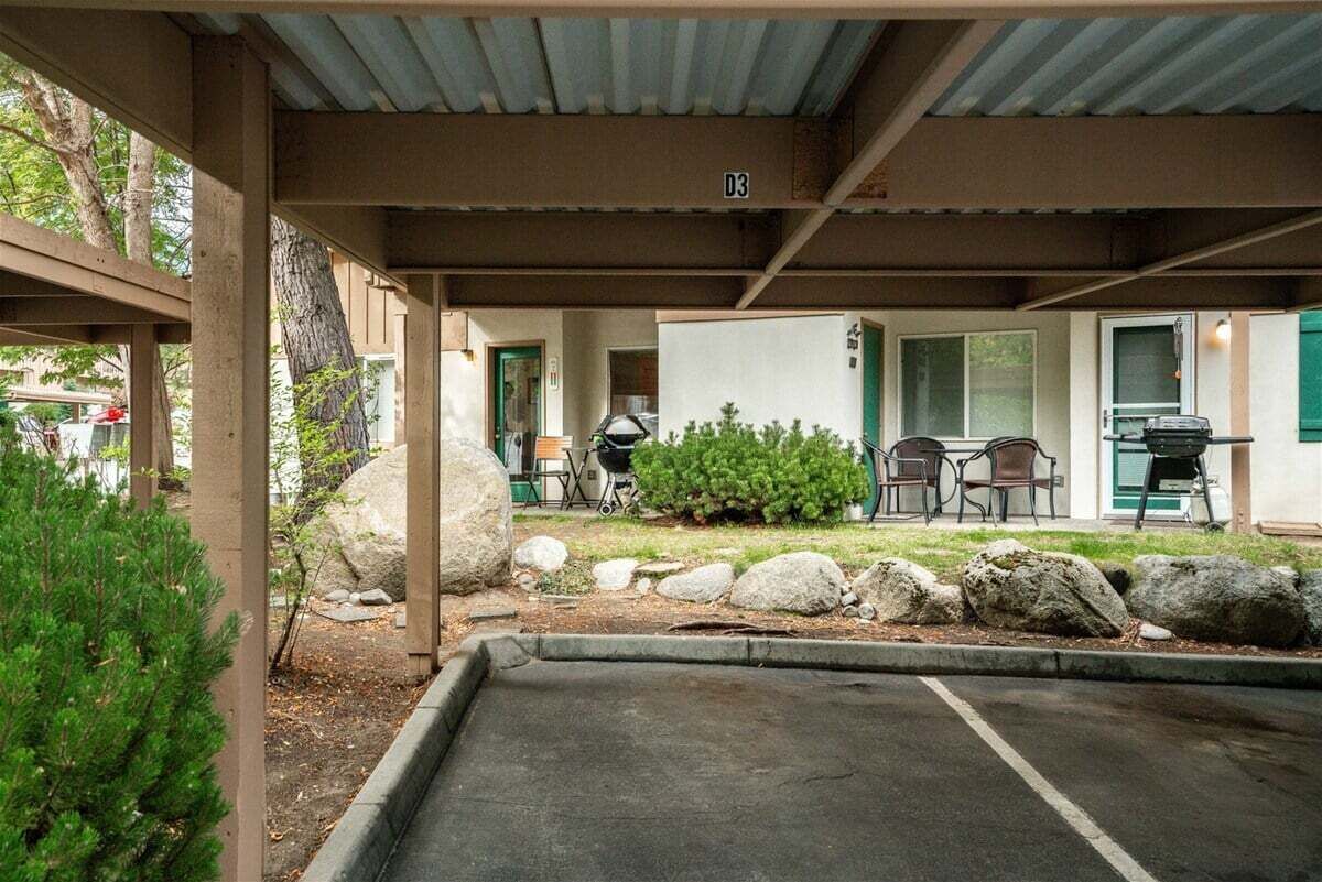 A covered outdoor area with a parking space, a grill, and a small garden with rocks and plants.