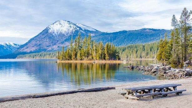 Une vue sur le lac, avec une montagne en arrière-plan, une plage de sable et une table de pique-nique.