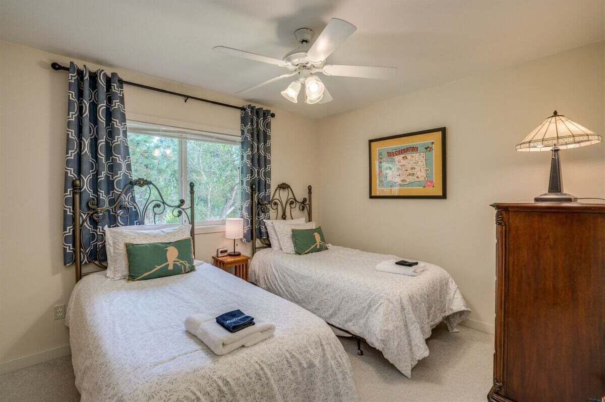 A room with two beds, a ceiling fan, a lamp, and a framed map on the wall.