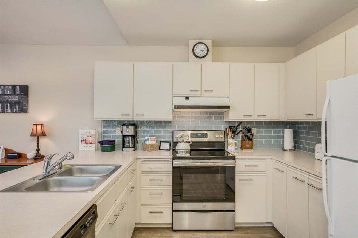 Eine moderne Küche mit weißen Schränken, einem Edelstahlbackofen, einer Kaffeemaschine und einer Uhr an der Wand.