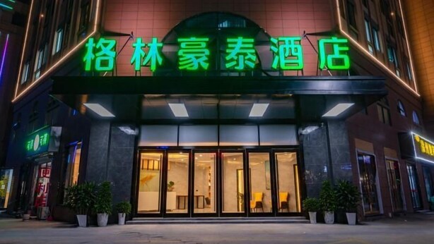 A hotel entrance with a neon sign, large glass doors, and potted plants. - Greentree Inn Zhejiang Jiaxing Honghe Town Business Hotel (Jiaxing)