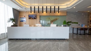 A modern reception area with a marble floor, a reception desk, a television mounted on the wall, and a large window with curtains. - Greentree Inn Zhejiang Jiaxing Honghe Town Business Hotel (Jiaxing)