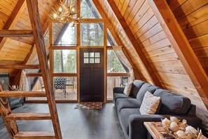 A cozy cabin with a loft bedroom, a dark wooden door, a gray sofa with decorative pillows, and a wooden staircase. - Pet-friendly A-Frame Near Plain & Leavenworth (Leavenworth)
