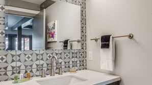 A modern bathroom with a geometric patterned tile backsplash, a large mirror, a sink with a faucet, and a towel rack. - Downtown Leavenworth King Studio - Parking + Balcony (Leavenworth)