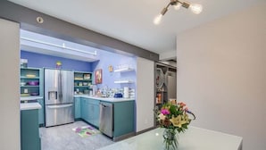 A modern kitchen with stainless steel appliances, teal cabinetry, and a dining area with a glass table and vase. - Downtown Leavenworth 2BR – Walk to Shops & Events (Leavenworth)