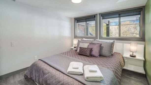A bedroom with a bed, two bedside lamps, a window, and a ceiling light. - Downtown Leavenworth 2BR – Walk to Shops & Events (Leavenworth)