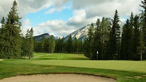 Un parcours de golf avec un bunker de sable, entouré d’arbres et de montagnes.