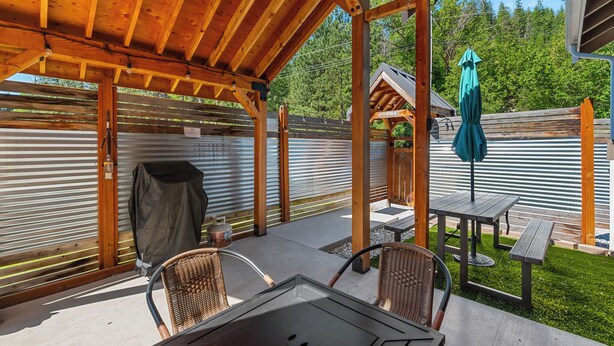 An outdoor patio with a wooden pergola, a table, chairs, a grill, and a green umbrella. - Cozy Mountain Retreat Near Leavenworth w/ Private Patio + BBQ (Leavenworth)