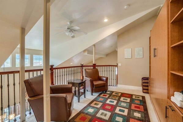 Une pièce spacieuse avec un plafond haut, un ventilateur de plafond, un escalier en bois et une grande armoire en bois.