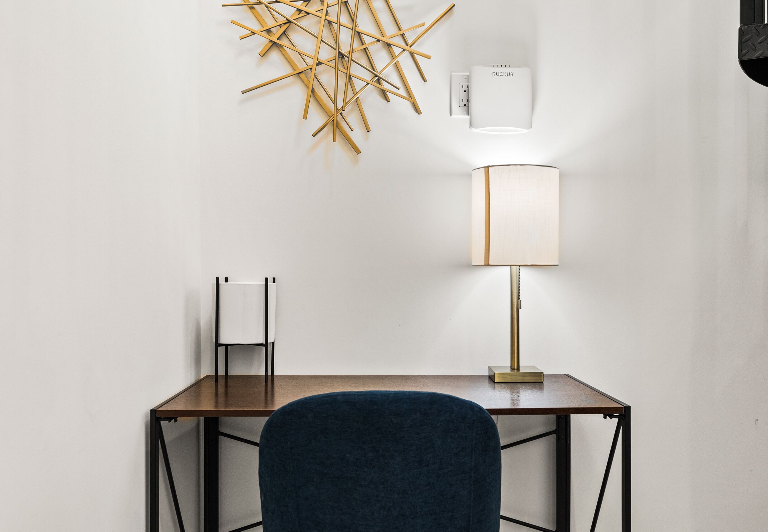 Et moderne skrivebord med en blå stol, en vægmonteret lampe og et geometrisk kunstværk på væggen.
