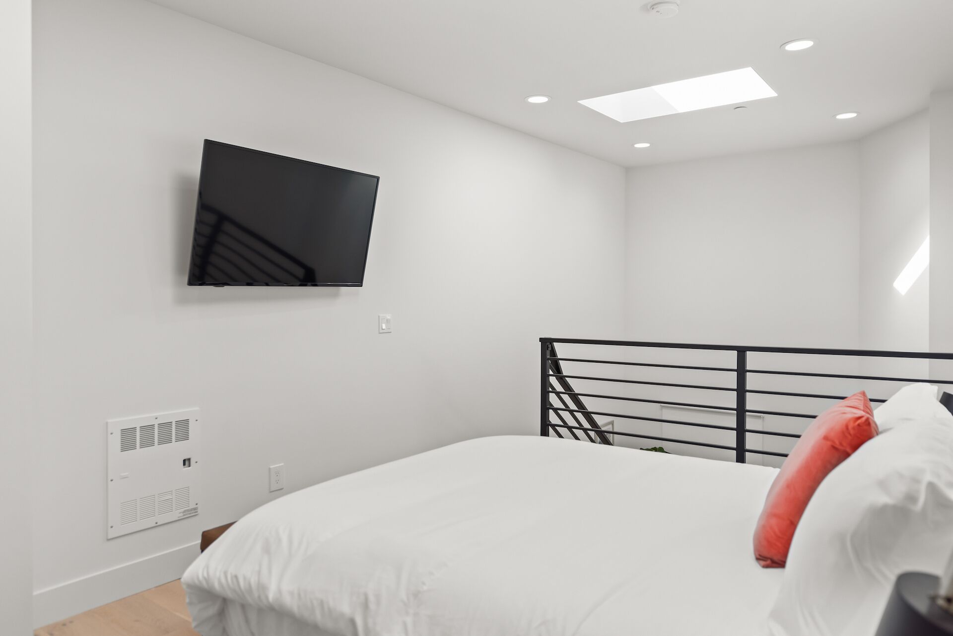 A bedroom with a bed, a TV mounted on the wall, a staircase, and a ceiling light.