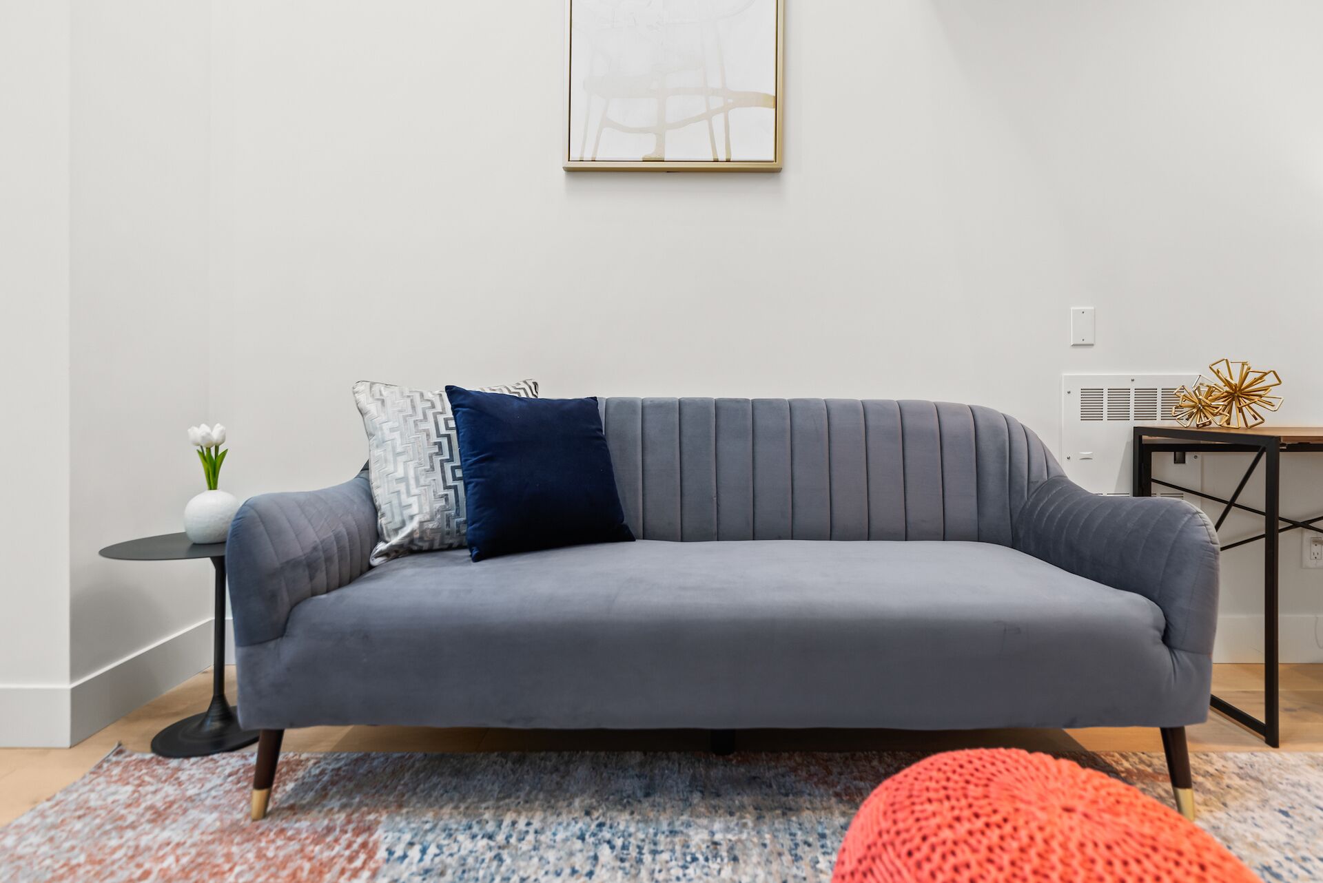 Una sala moderna con un sofá gris, una mesita redonda con un florero y una pieza decorativa sobre una mesita auxiliar.