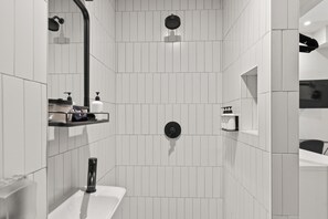 A modern bathroom with white tiles, a black showerhead, a sink, and a mirror.