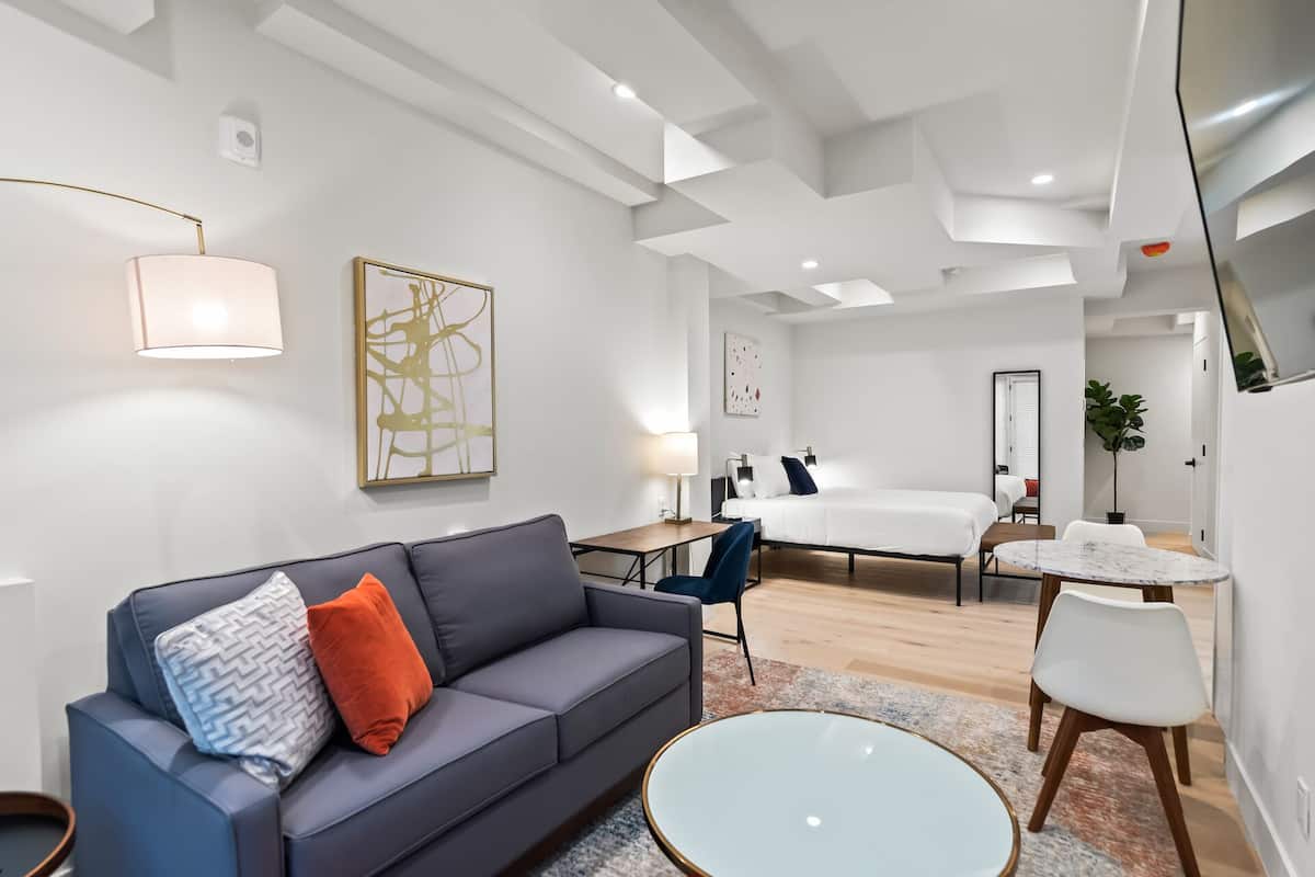 Moderni hotellihuone, jossa on sohva, pyöreä pöytä, sänky ja työpöytä.