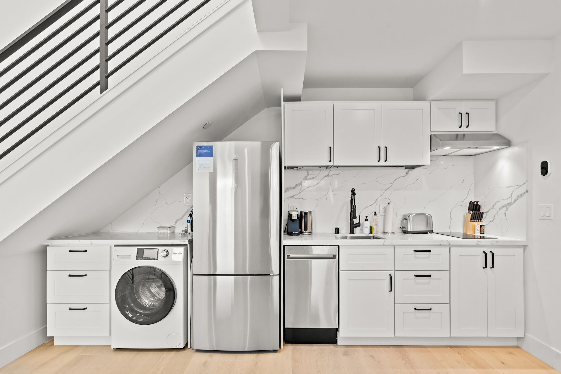 Cocina compacta con armarios blancos, refrigerador de acero inoxidable, lavadora y lavavajillas.