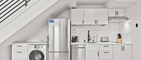 Cocina compacta con armarios blancos, refrigerador de acero inoxidable, lavadora y lavavajillas.