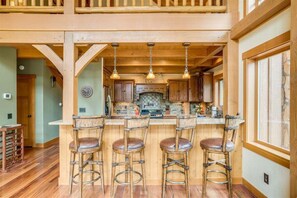 A spacious kitchen with wooden bar stools, a large island, and hanging pendant lights. - Norge Haus - Riverfront Extraordinary Home (Leavenworth)