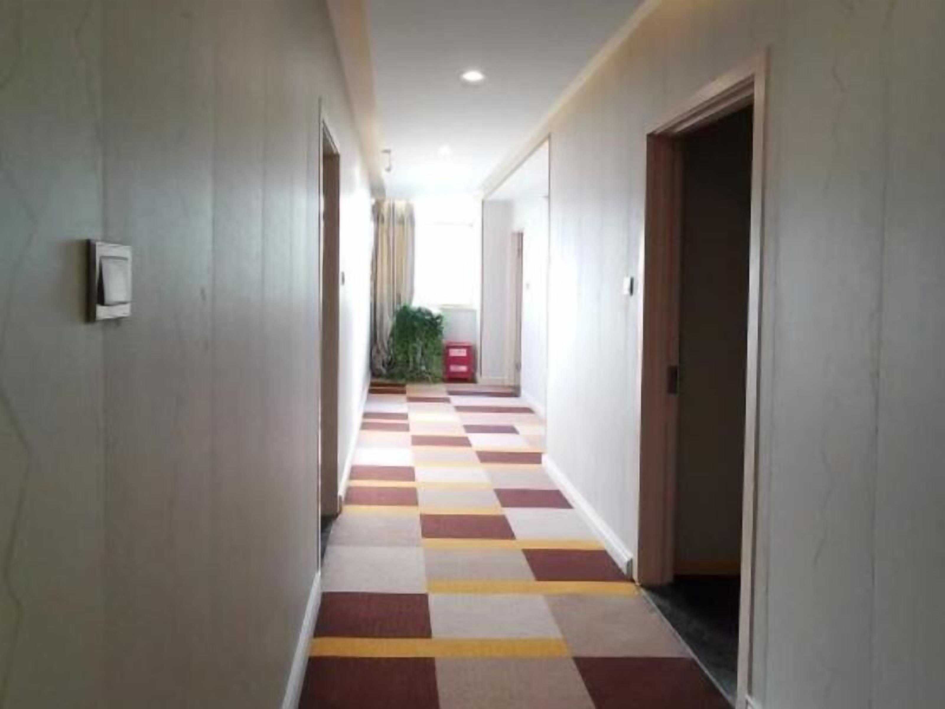 A hallway with a checkered floor pattern, doors on both sides, and a plant in the distance.