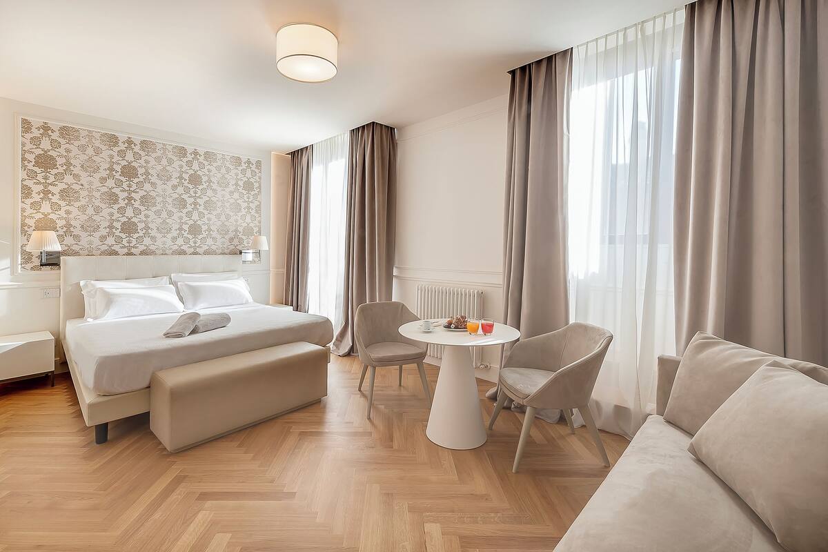 Ein Hotelzimmer mit einem Bett, einer Sitzecke mit Tisch und einem großen Fenster mit Vorhängen.