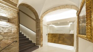 A hotel lobby with a marble floor, a staircase with dark steps, and a reception desk with a gold finish. - Asisium Boutique Hotel (Assisi)