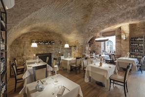 A restaurant with stone walls and vaulted ceilings, tables set with white tablecloths and wine glasses. - Asisium Boutique Hotel (Assisi)