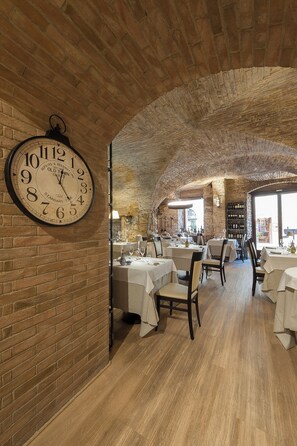 A restaurant with brick walls, a large clock, and tables set for dining. - Asisium Boutique Hotel (Assisi)