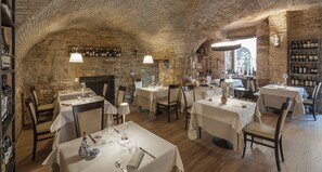 A restaurant with stone walls, multiple tables set for dining, and wine bottles on shelves. - Asisium Boutique Hotel (Assisi)