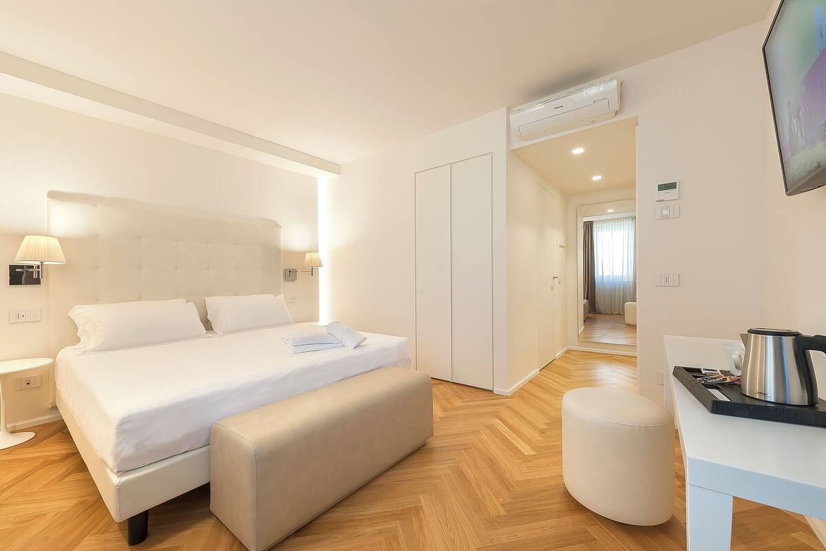 Ein modernes Hotelzimmer mit einem großen Bett, Nachttischen, einem Schreibtisch mit Wasserkocher und einem Fernseher.