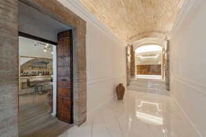 A hotel corridor with a brick wall, a wooden cabinet, a marble floor, and a view into a room with a bed and a bathroom. - Asisium Boutique Hotel (Assisi)