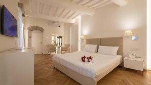 A hotel room with a large bed, a bedside table with a lamp, a TV mounted on the wall, and a wooden floor. - Asisium Boutique Hotel (Assisi)