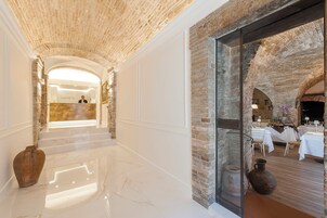 Vestíbulo de hotel con techo de piedra, una recepción y un área de comedor visible a través de un panel de vidrio.