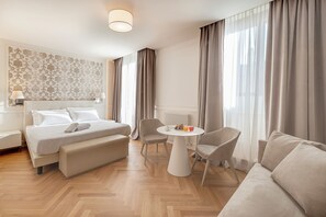 A hotel room with a bed, a seating area with a table, and a large window with curtains. - Asisium Boutique Hotel (Assisi)
