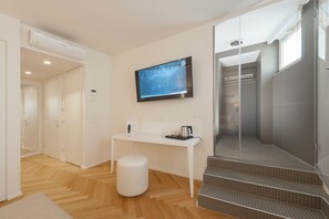 Un baño moderno con ducha, inodoro y lavabo. Hay un banco blanco y una pequeña mesa con un hervidor y una taza.