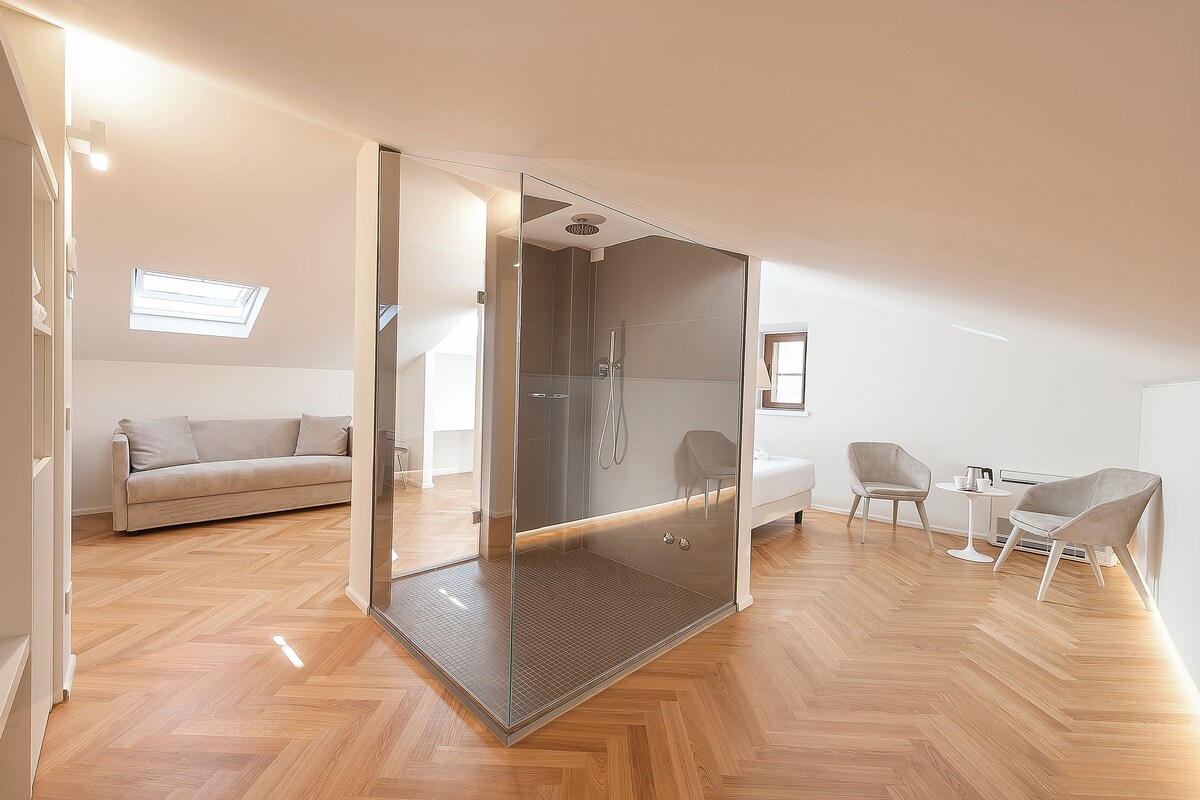 A modern, well-lit room with a glass-enclosed shower, a sofa, and a small table with chairs.