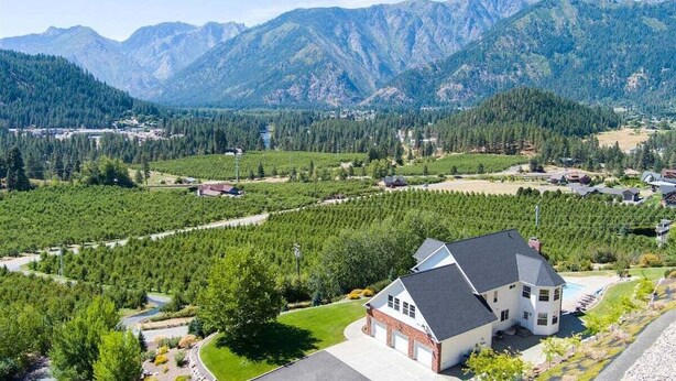 Une maison avec une grande allée, entourée d’une zone boisée et avec des montagnes en arrière-plan.