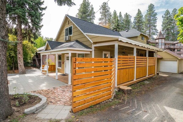A two-story cabin with a covered porch, a fenced yard, and a mountain backdrop.