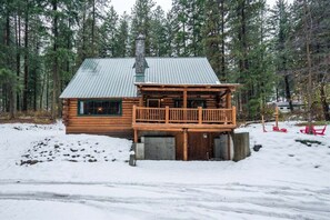 A log cabin with a metal roof, a wooden deck, and a chimney.