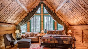 Une chambre dans un chalet en rondins, avec un lit en mezzanine, une chaise, une petite table et une fenêtre avec des rideaux.