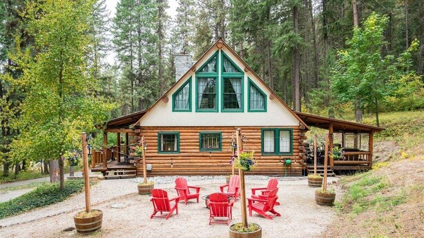 Une cabane en rondins avec un toit triangulaire, des fenêtres vertes et une terrasse dotée de chaises rouges.