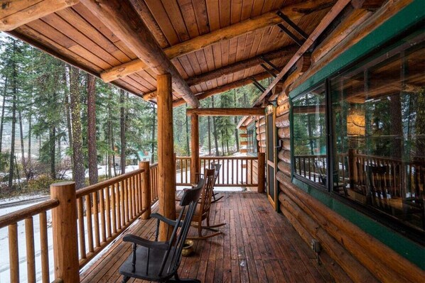 A wooden deck with chairs, a railing, and a view of trees.