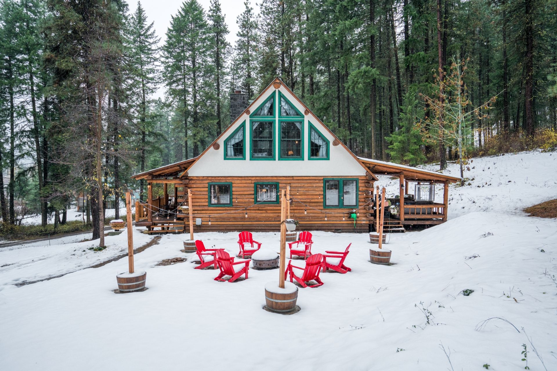 A cabin with a large porch and red chairs, surrounded by snow and trees.