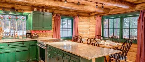 Cocina de estilo cabaña con armarios verdes, encimera de granito y piso de madera.