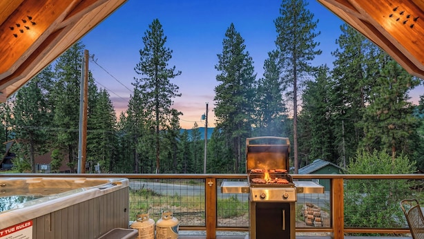Une terrasse en bois avec un jacuzzi, un barbecue et des bouteilles de propane.