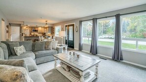 Ein geräumiges Wohnzimmer mit grauem Sofa, einem Couchtisch und Blick auf die Küche und den Garten.